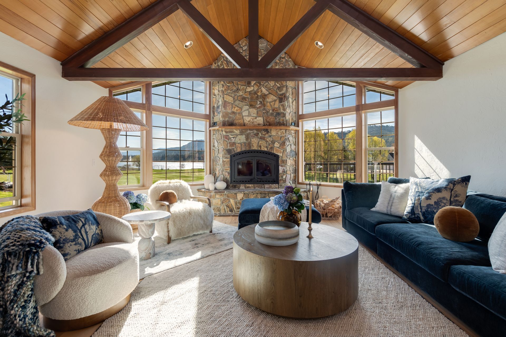 Cozy living room with vaulted wood ceiling, stone fireplace, blue sofa, and large windows with mountain view