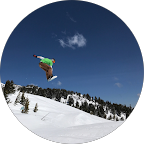 Snowboarder midair over a snowy mountain slope under a blue sky.