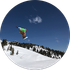 Snowboarder jumps in the air against a blue sky with snowy mountain in the background.