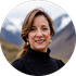 Woman with shoulder-length brown hair smiling, wearing a black turtleneck and earrings, snowy mountains in the background.