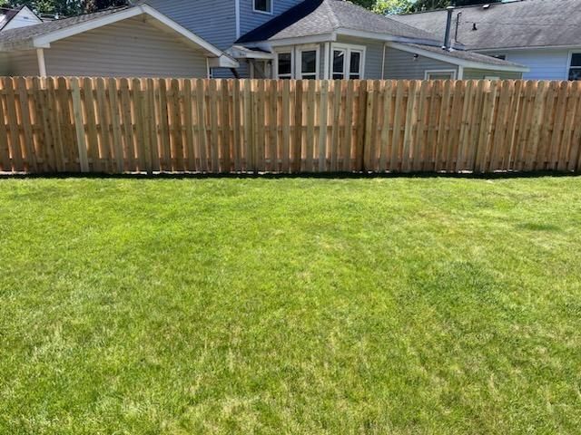 Lawn with green grass in front of a wood fence surrounding a house.
