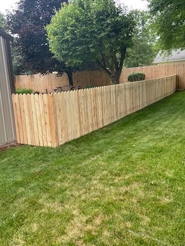 Wooden fence in a grassy yard, with trees and a shed in the background.