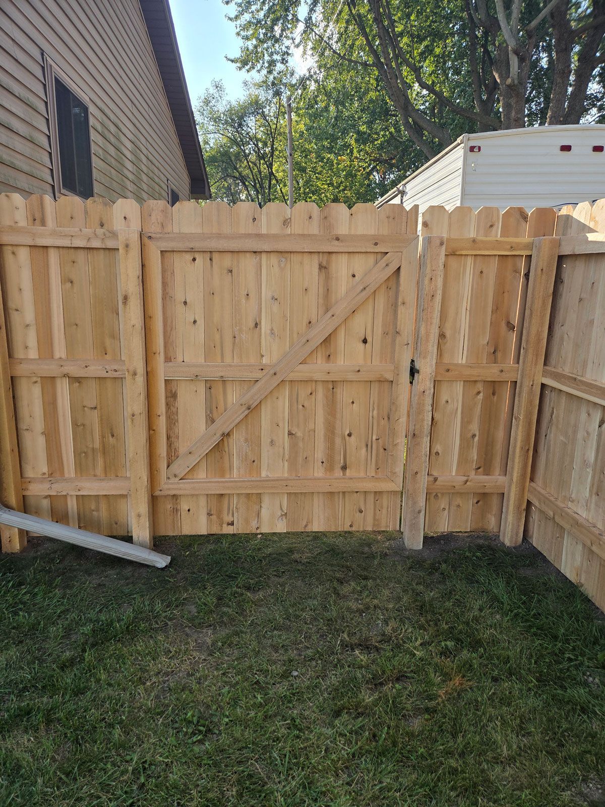 Wooden fence with gate in grassy yard. A diagonal brace reinforces the gate.