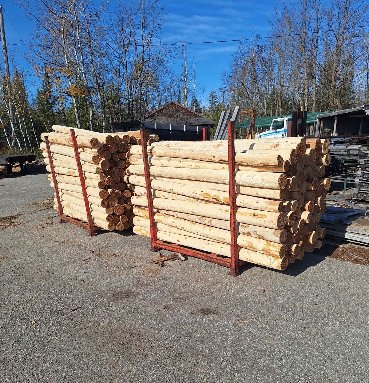 Stacks of wooden logs in metal racks on gravel.