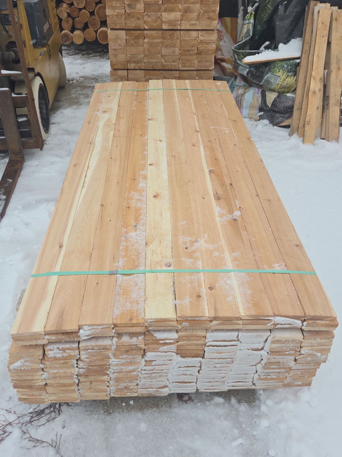 Stack of wooden planks bound with green straps, outdoors in the snow.