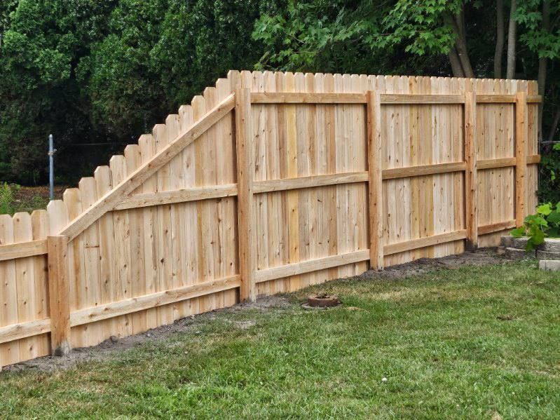 Wooden fence along a grassy yard, partially obscuring a tree line.