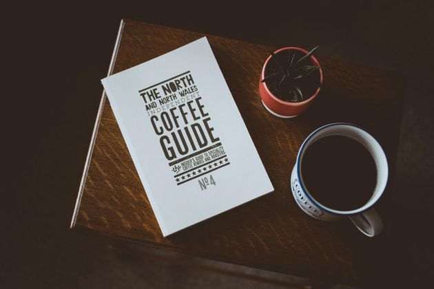 A coffee guide is sitting on a wooden table next to a cup of coffee.