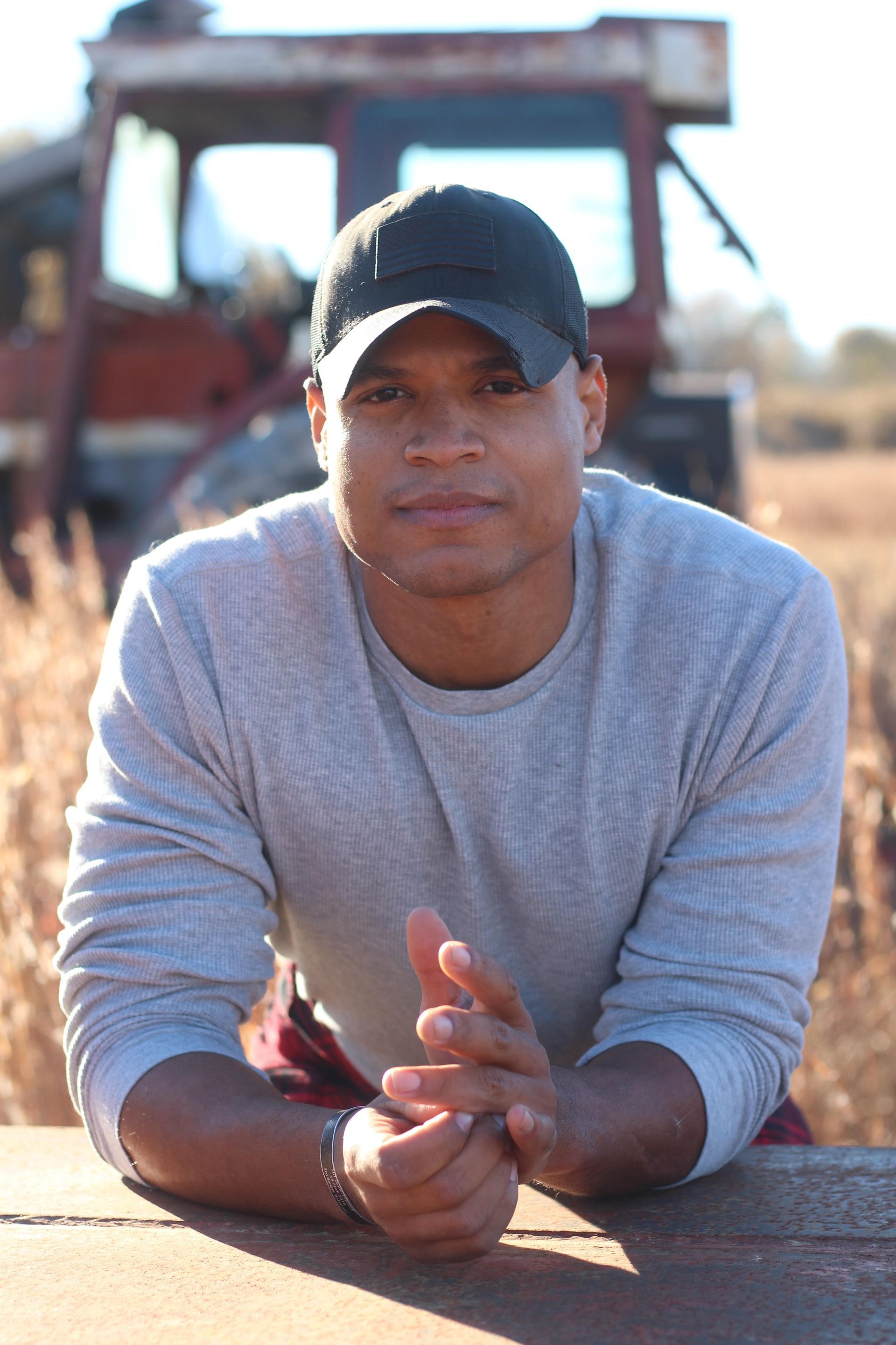A man in a gray shirt is standing in a field with mountains in the background.