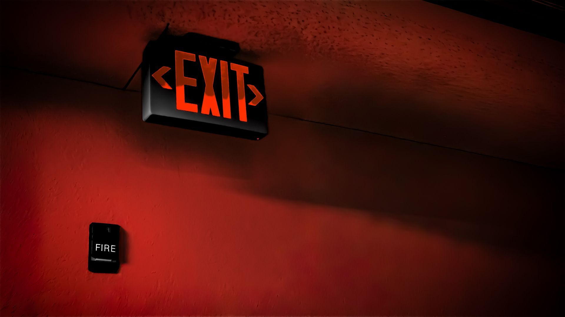 A glowing EXIT sign and a black fire alarm pull. A glowing EXIT sign and a black fire alarm pull.
