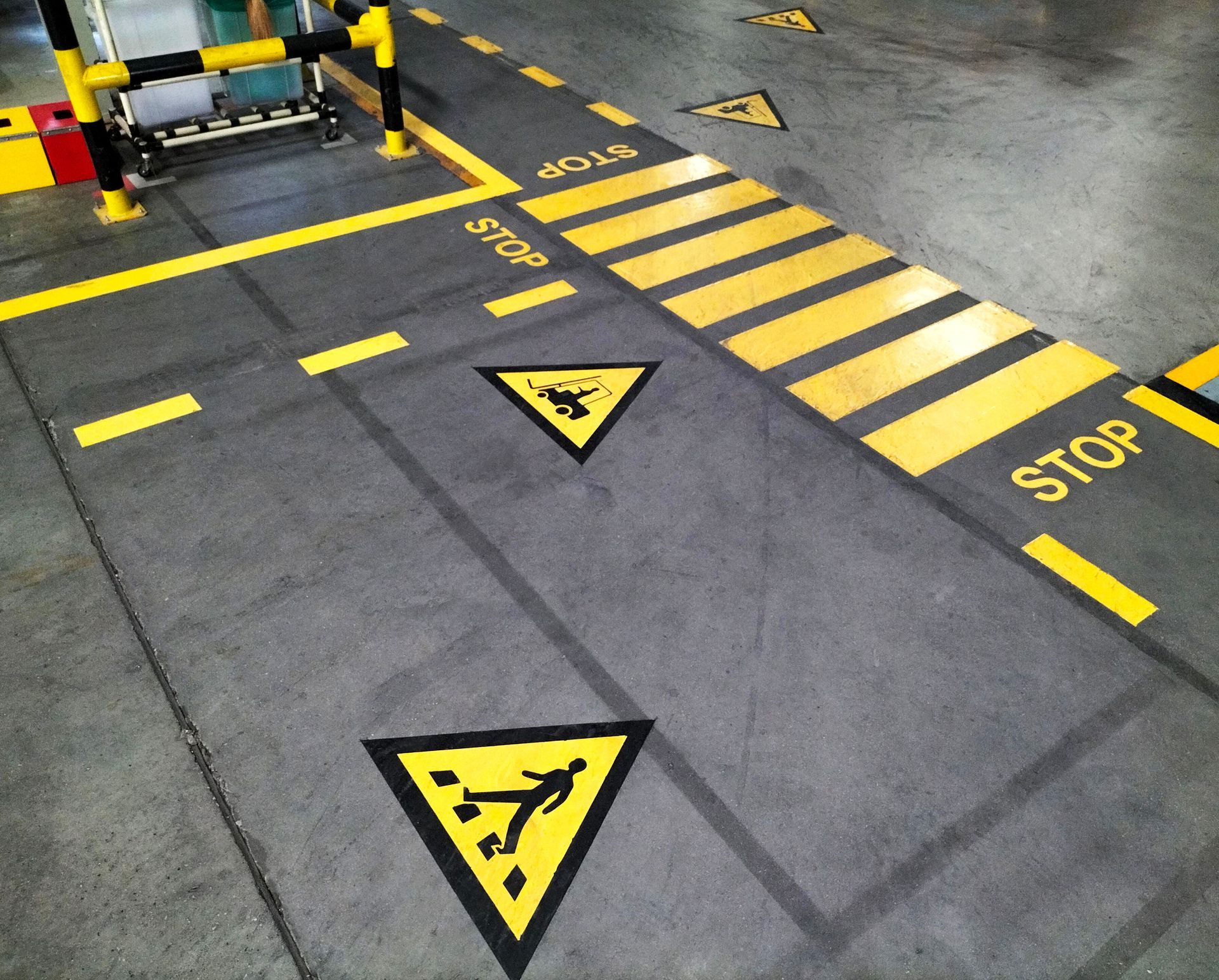 A warehouse floor with yellow stop lines, caution symbols, and safety markings painted on concrete