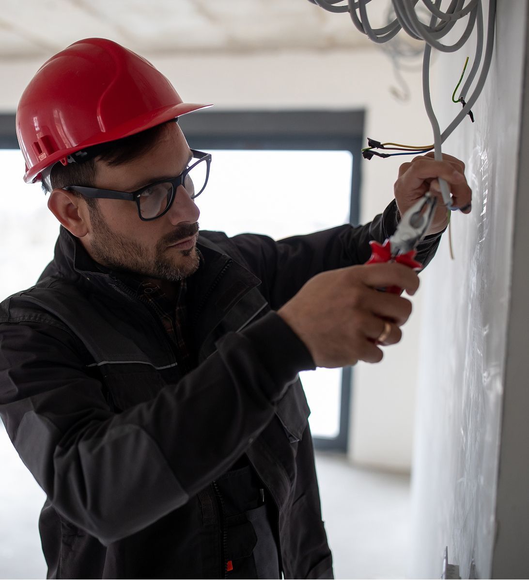 A man wearing a red hard hat is working on wires