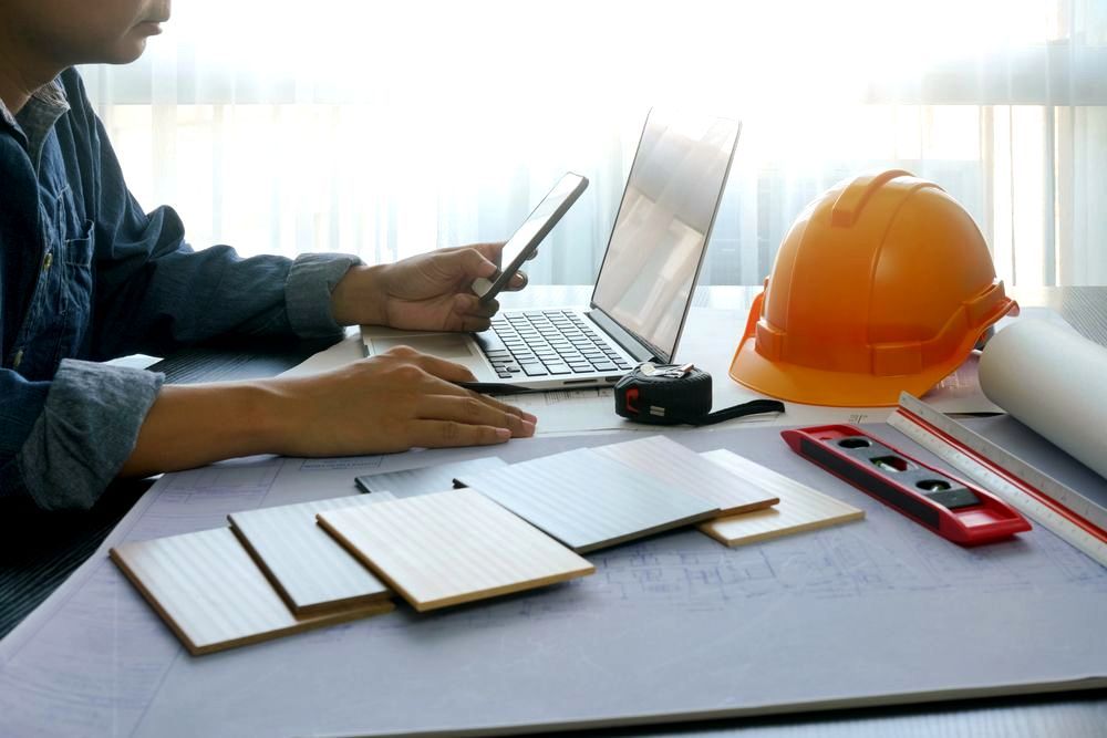 A man is sitting at a table using a laptop and a cell phone. A man is sitting at a table using a laptop and a cell phone.