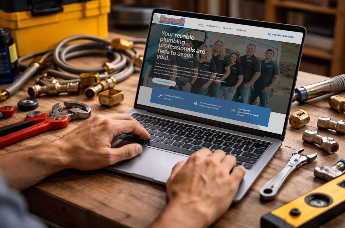 Man using laptop showcasing plumbing services, surrounded by tools on a wooden surface.