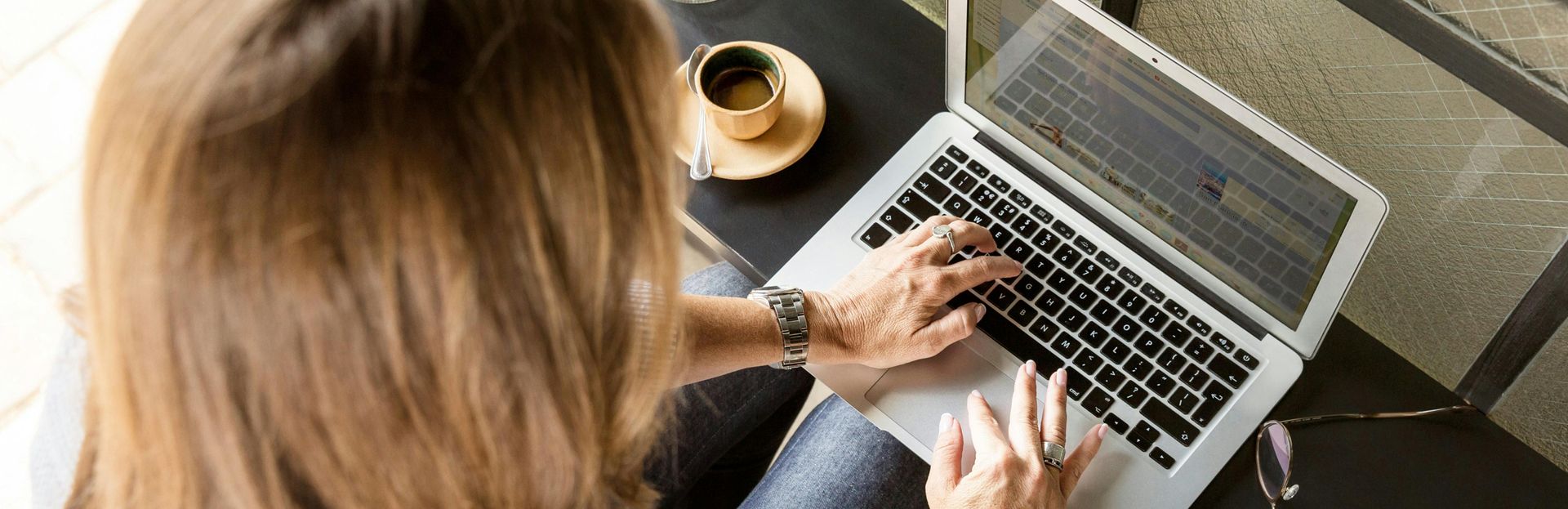 A woman is typing on a laptop computer while sitting at a table with a cup of coffee.