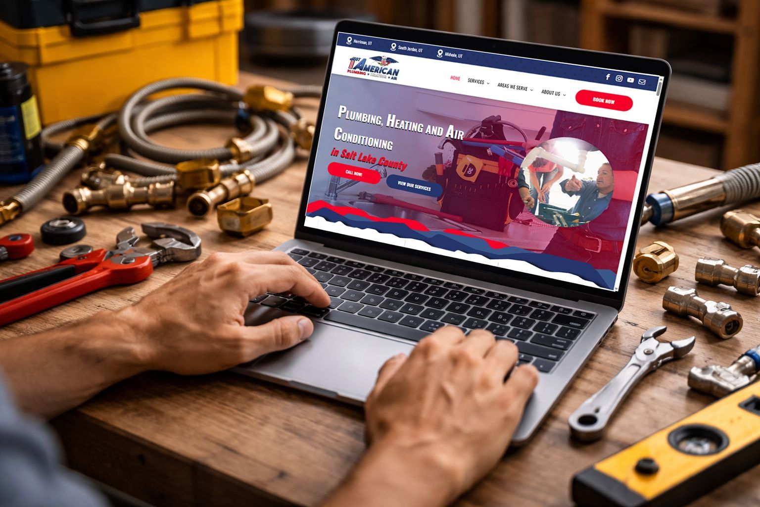 Man using laptop showcasing plumbing services, surrounded by tools on a wooden surface.