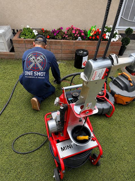 Technician kneeling on grass beside a red mobile machine, working near flower beds and tools outdoors.