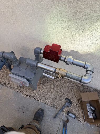 Outdoor gas meter and piping beside a wall, with a red shutoff valve and tools on the ground.