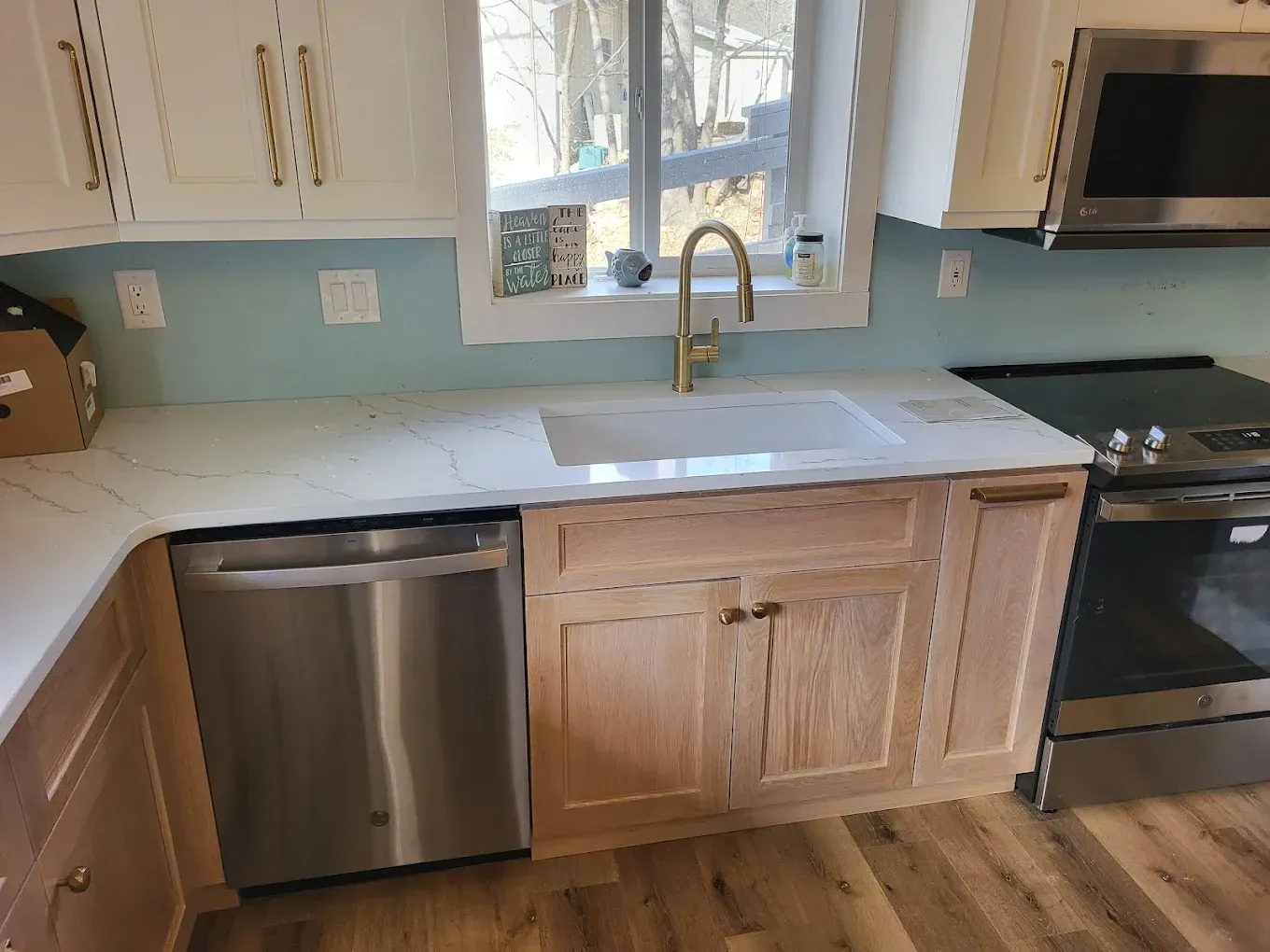 Kitchen with light wood cabinets, white countertops, stainless steel appliances, and a gold faucet.