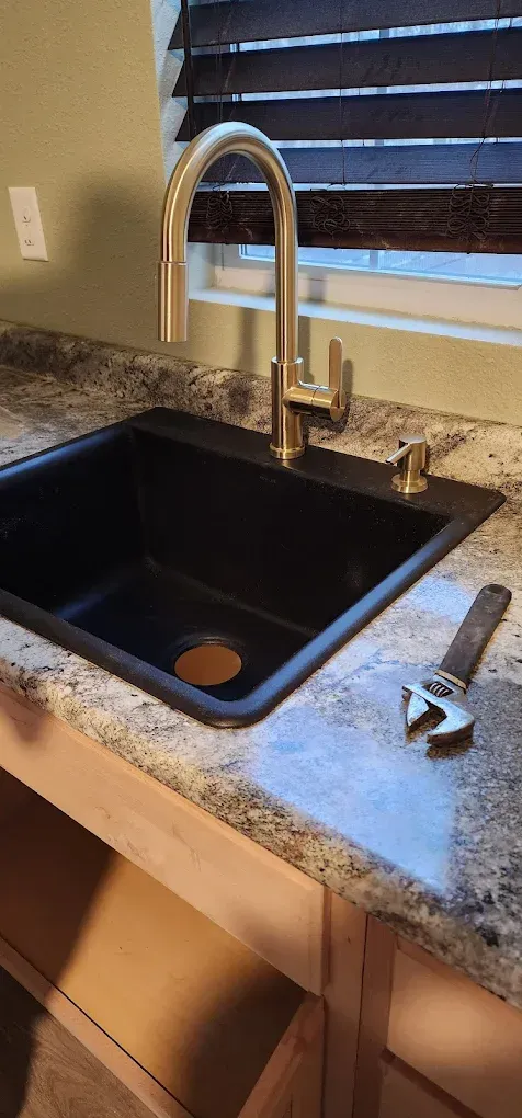 A kitchen sink with a faucet and adjustable wrench on the countertop.