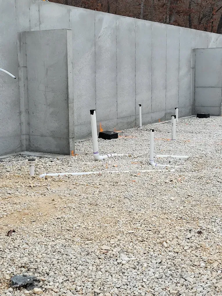 White PVC pipes protruding from gravel floor against a concrete wall.