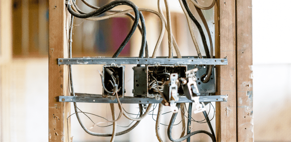 Electrical wiring and boxes exposed within a wooden frame, likely during construction.