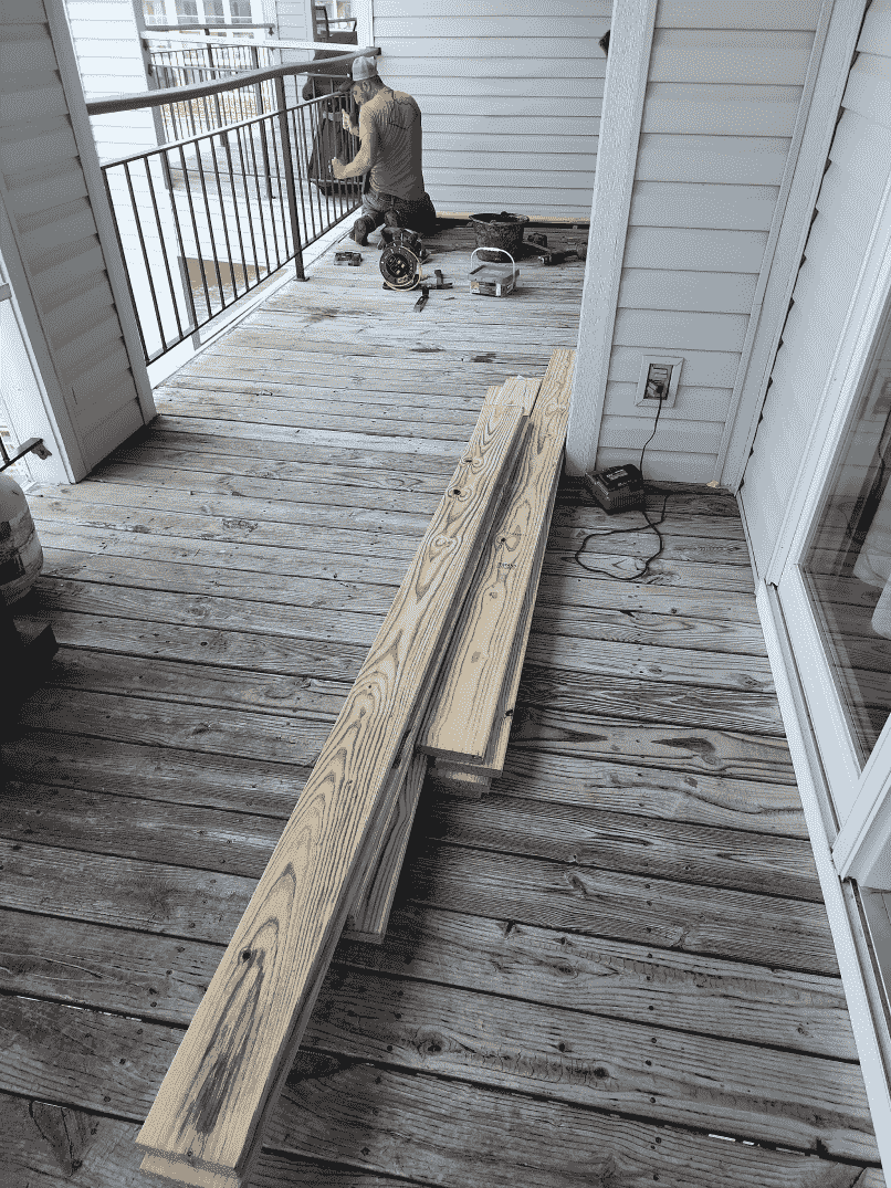 A balcony with old wood flooring being replaced. New planks are stacked nearby.