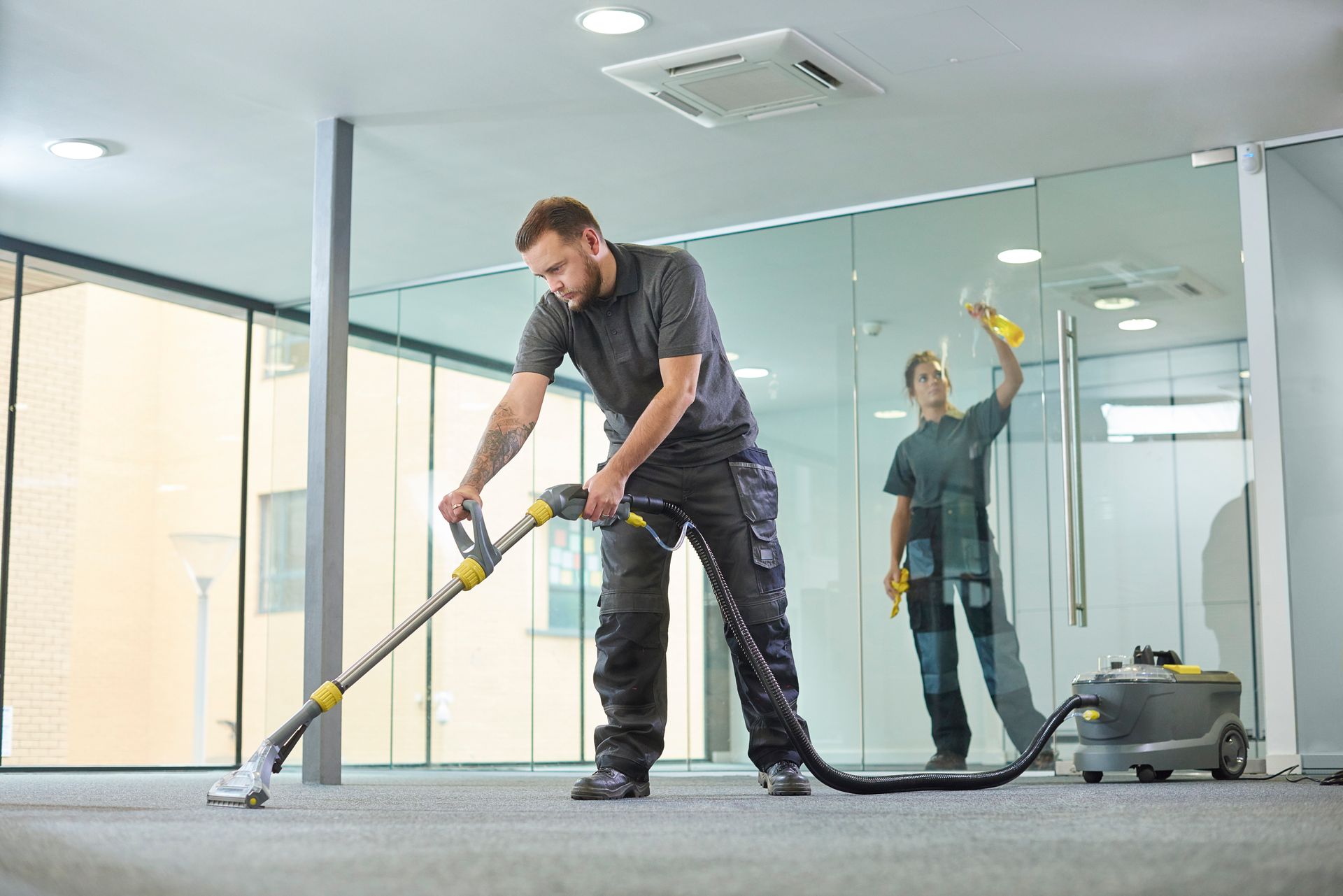 A male contractor providing commercial carpet cleaning service, with female cleaning glass behind.