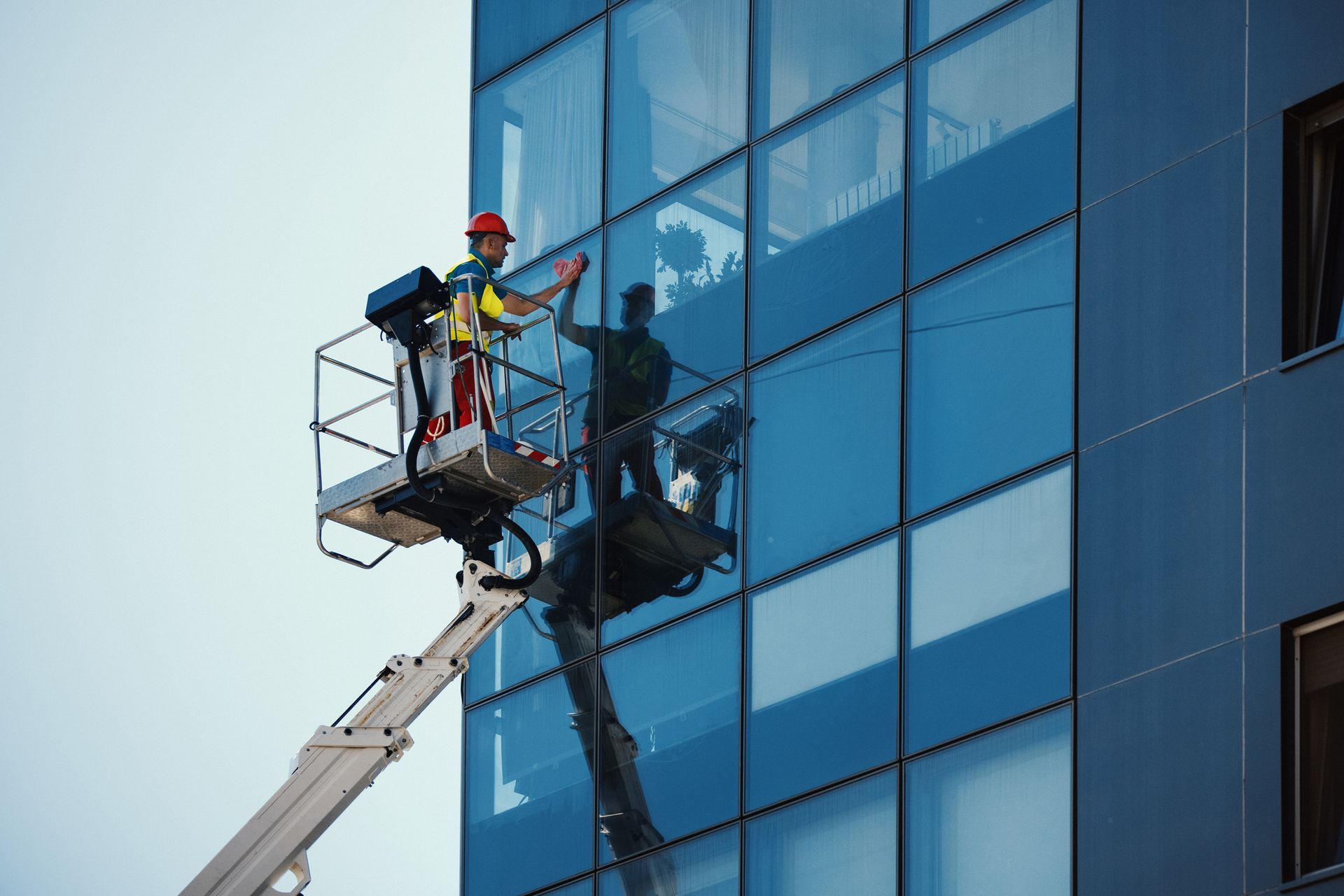 Side view of a man washing windows on a commercial building. He's standing inside construction platf