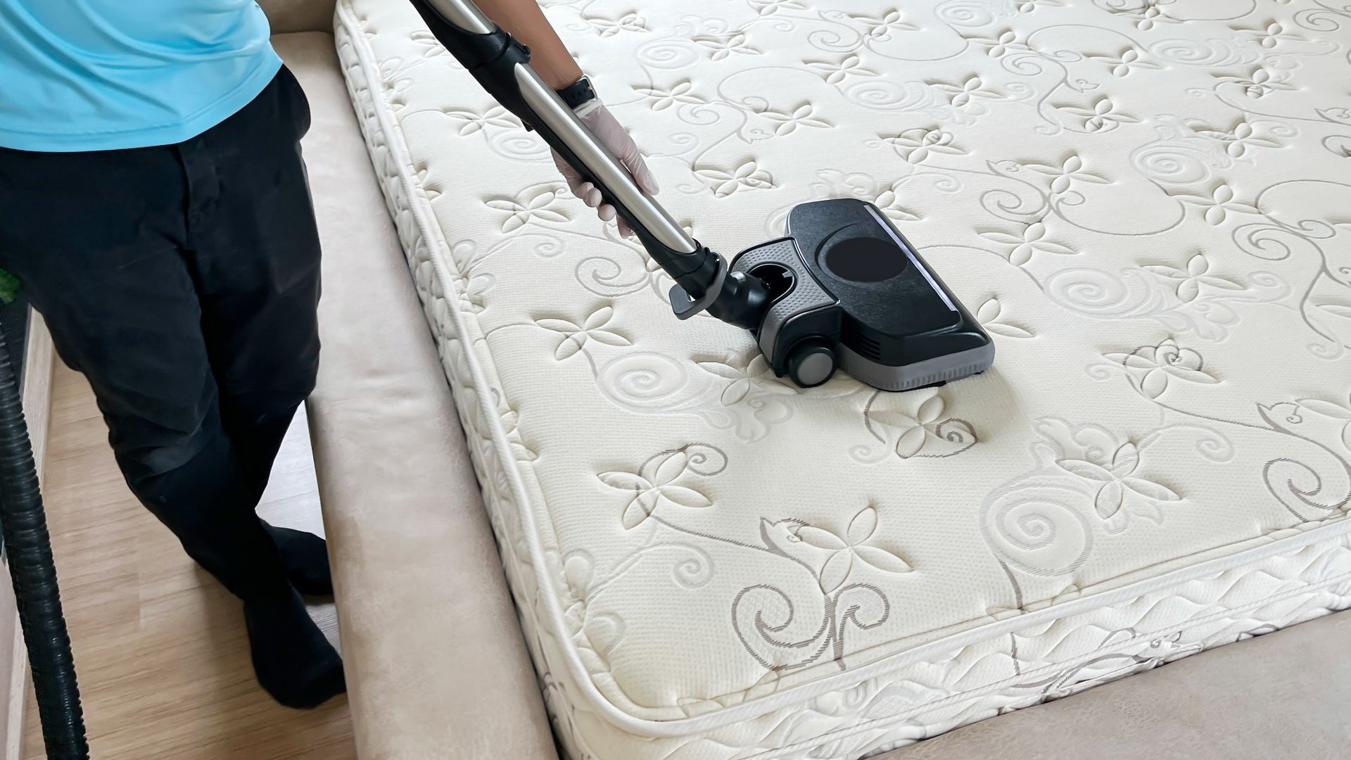 Commercial cleaning worker uses an industrial vacuum to clean a bed mattress.