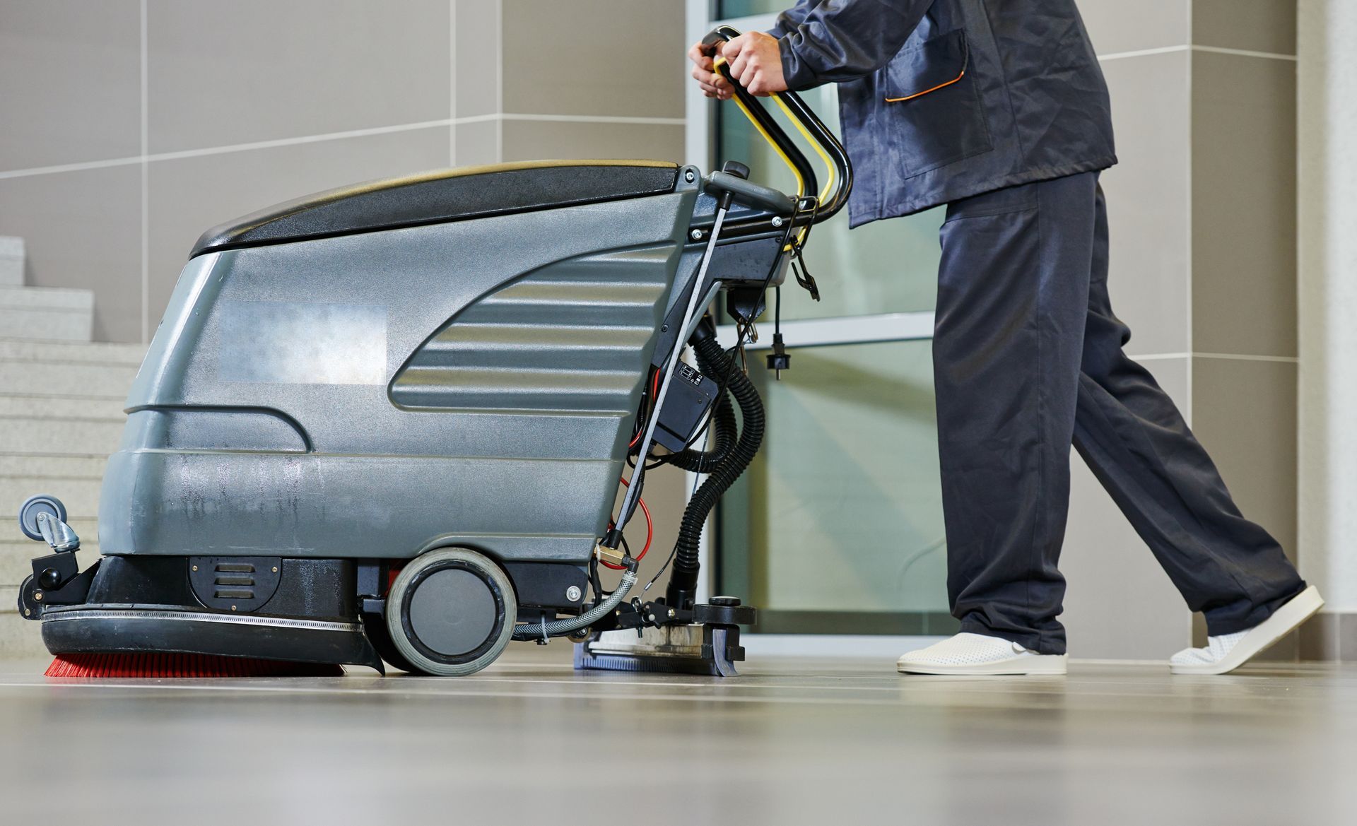 Person operating an industrial floor cleaner in a hallway with a shiny floor.