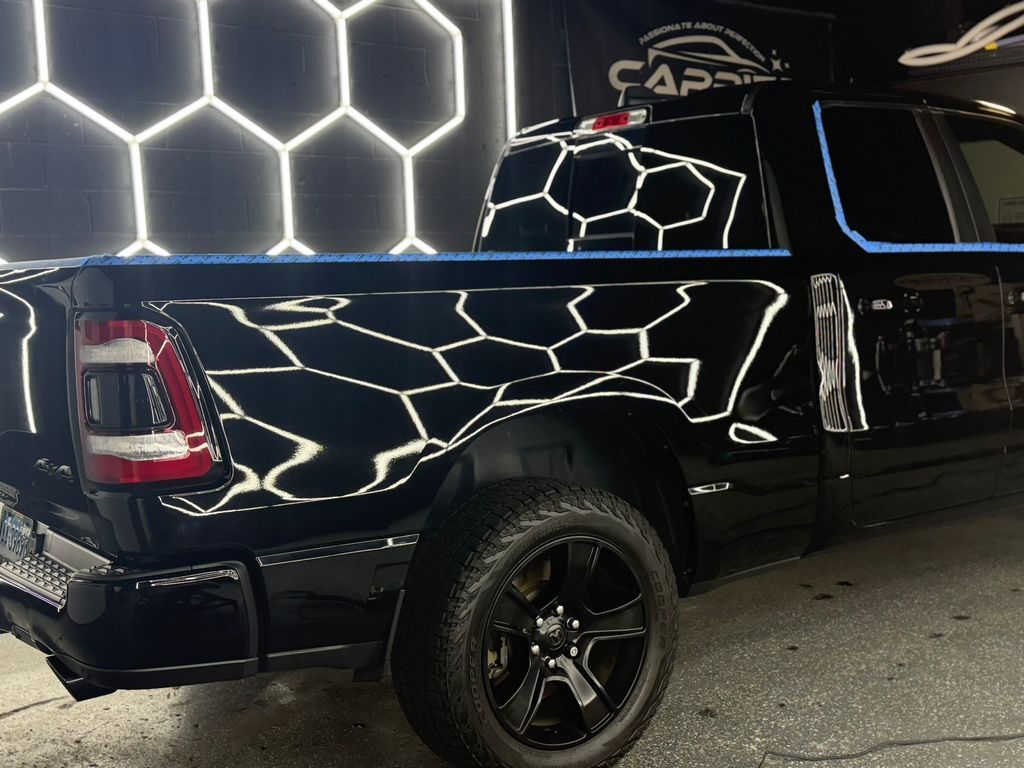Black pickup truck reflecting geometric shapes under bright lights in a shop.