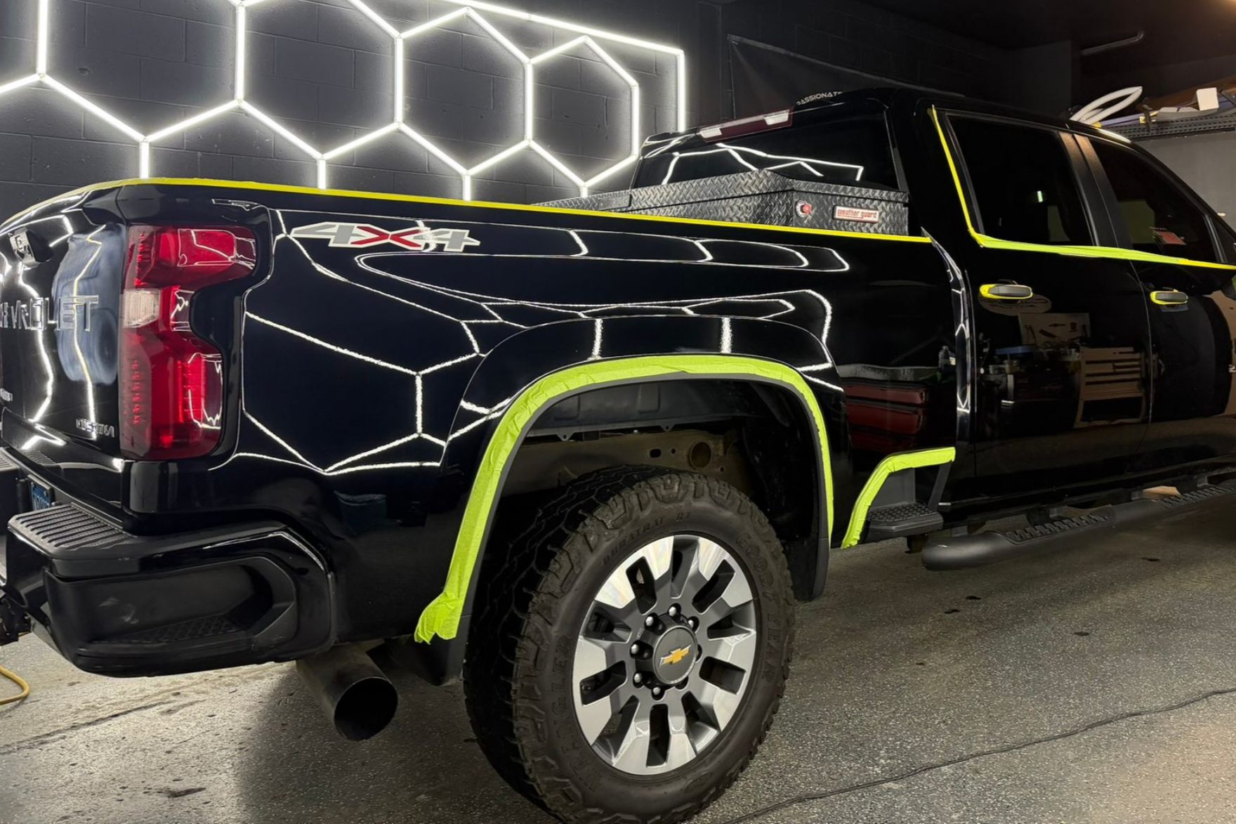 Black pickup truck with protective tape in a shop, honeycomb light in the background.