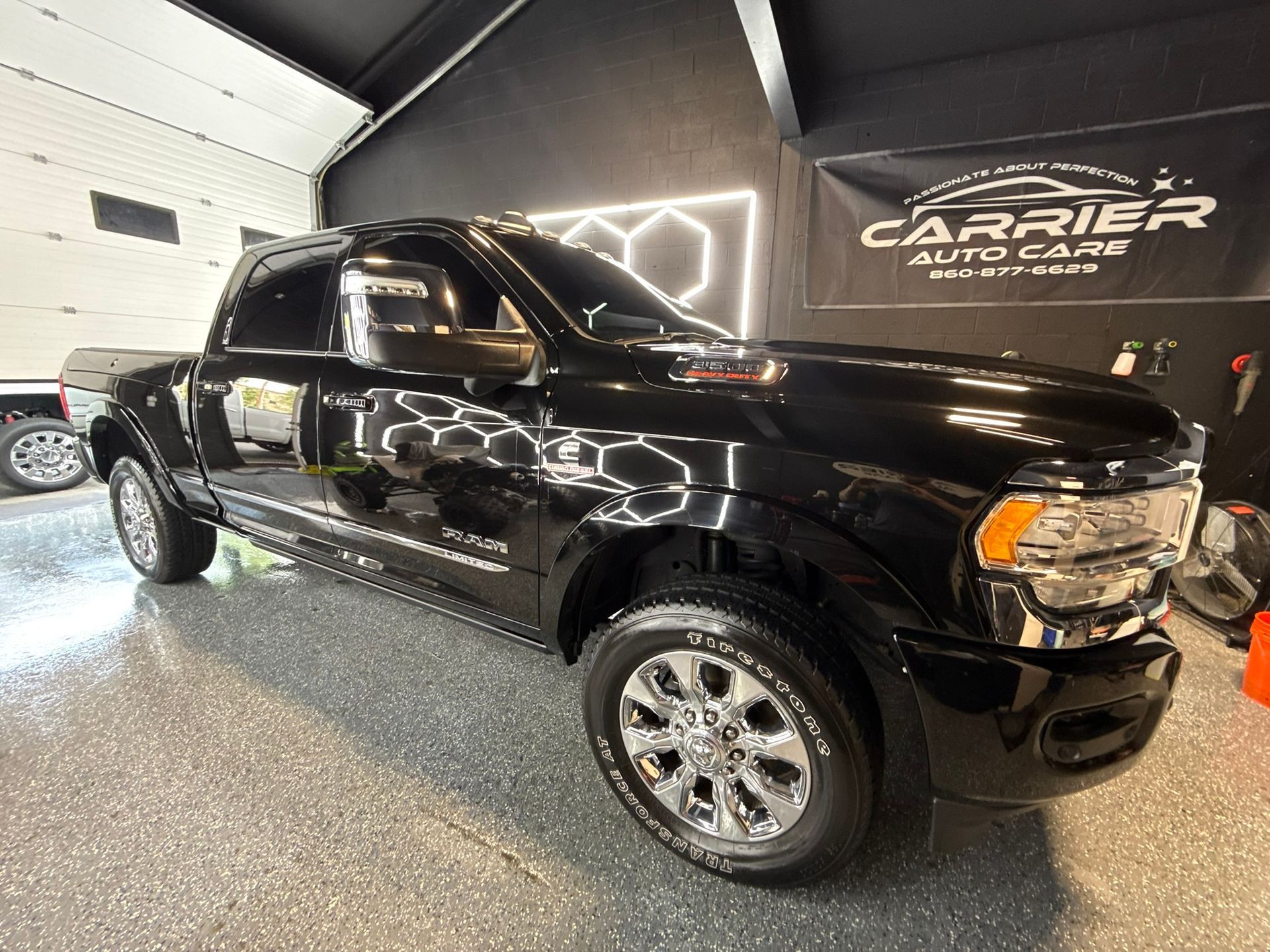 Person using a polisher on a black car's side panel near a tire, likely detailing the vehicle.