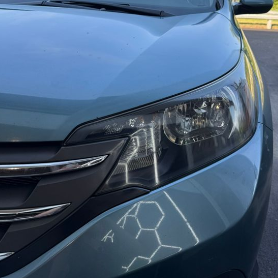 Close-up of a blue car's headlight and front end, with a hexagonal pattern reflection on the hood.