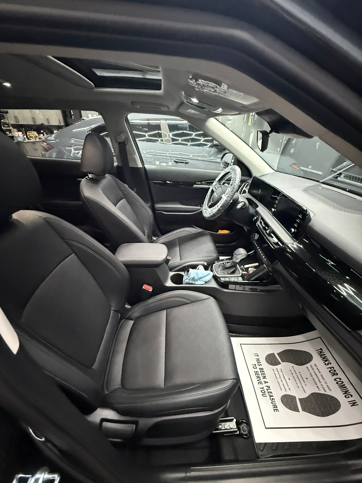 Interior view of a black Kia Seltos SUV. Gray and black leather seats, sunroof, steering wheel, and dashboard visible.