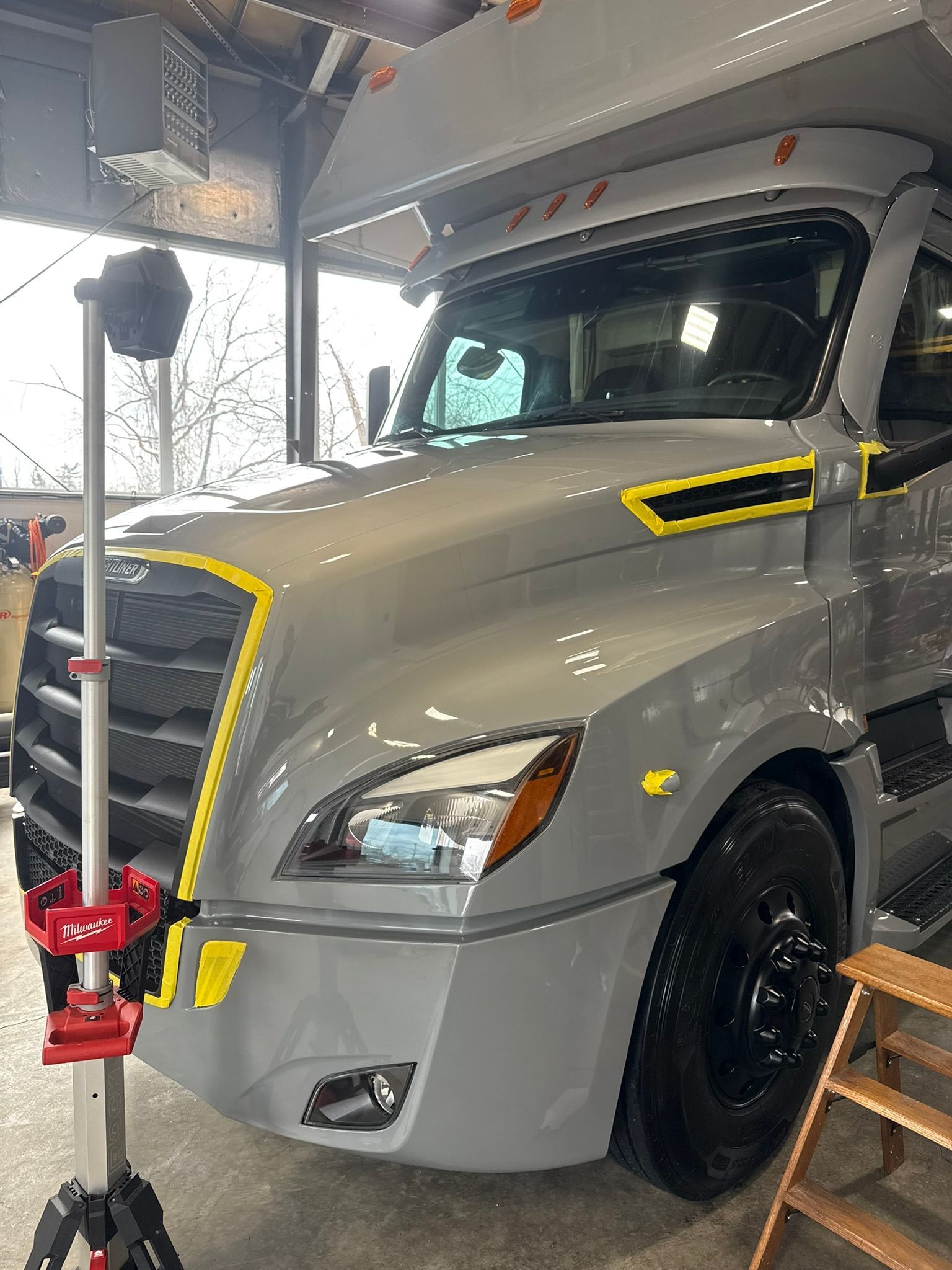 A gray truck being worked on with a spotlight. The hood has yellow tape.