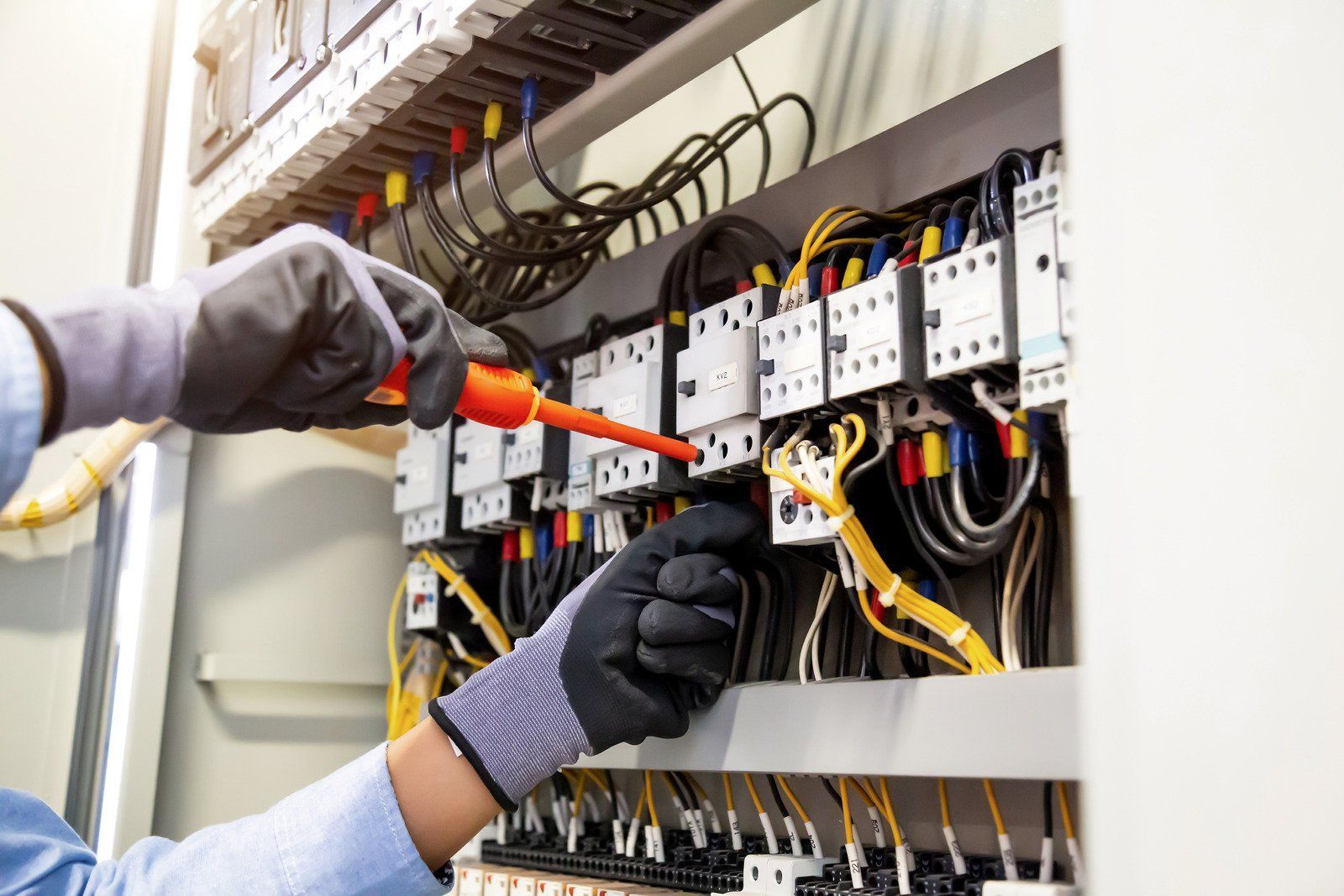 Electrician working on electrical panel, wearing gloves, using a screwdriver.