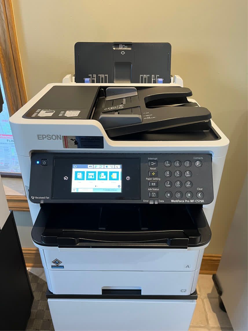 White Epson printer with touchscreen and document feeder on a wood floor.