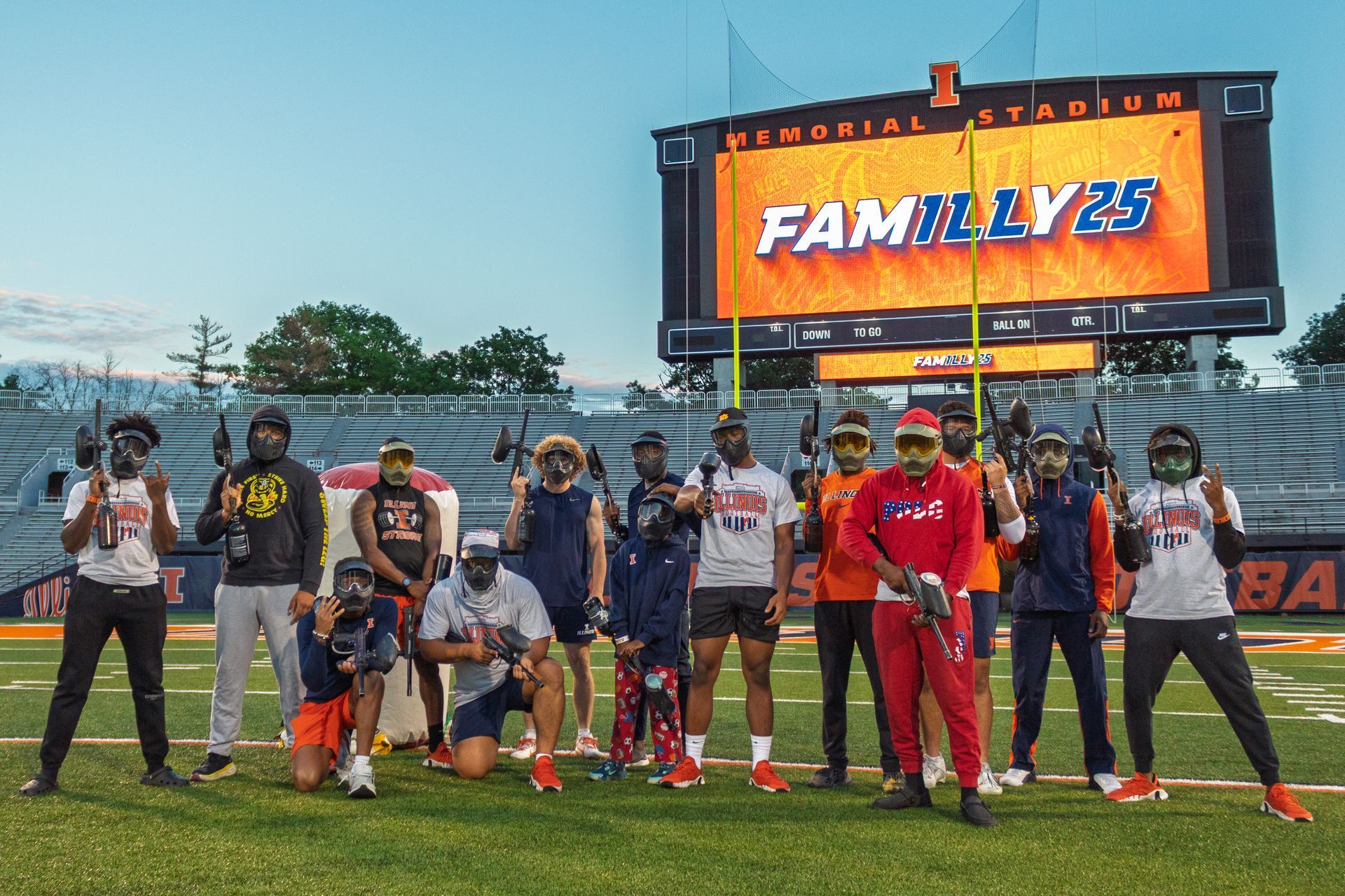 Illini football team posing with paintball guns in front of a stadium sign that says