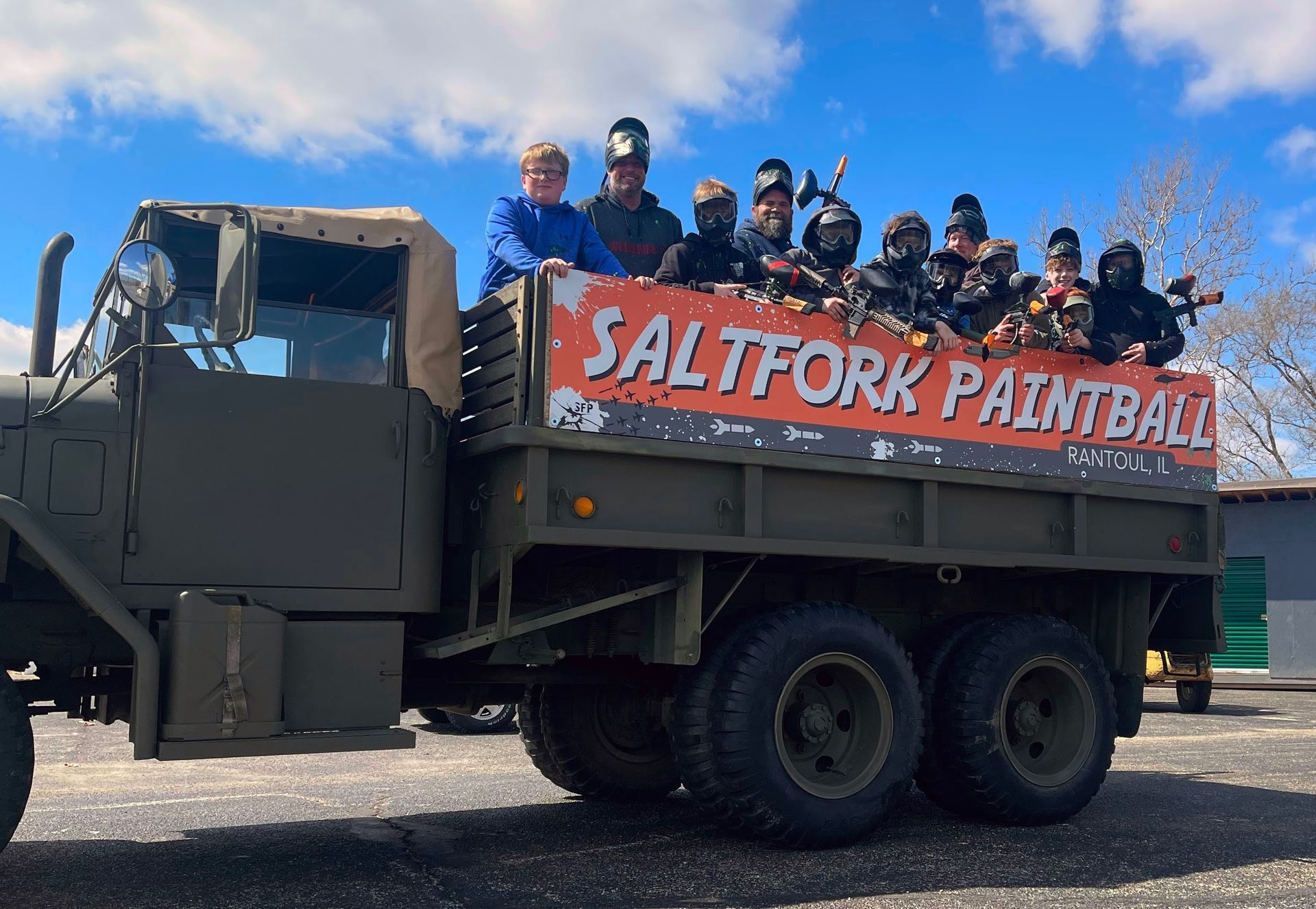 Group of people in paintball gear riding on a military truck with