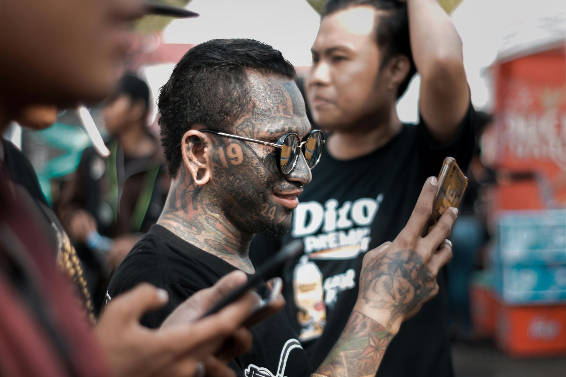 A man with tattoos on his face is looking at his cell phone.