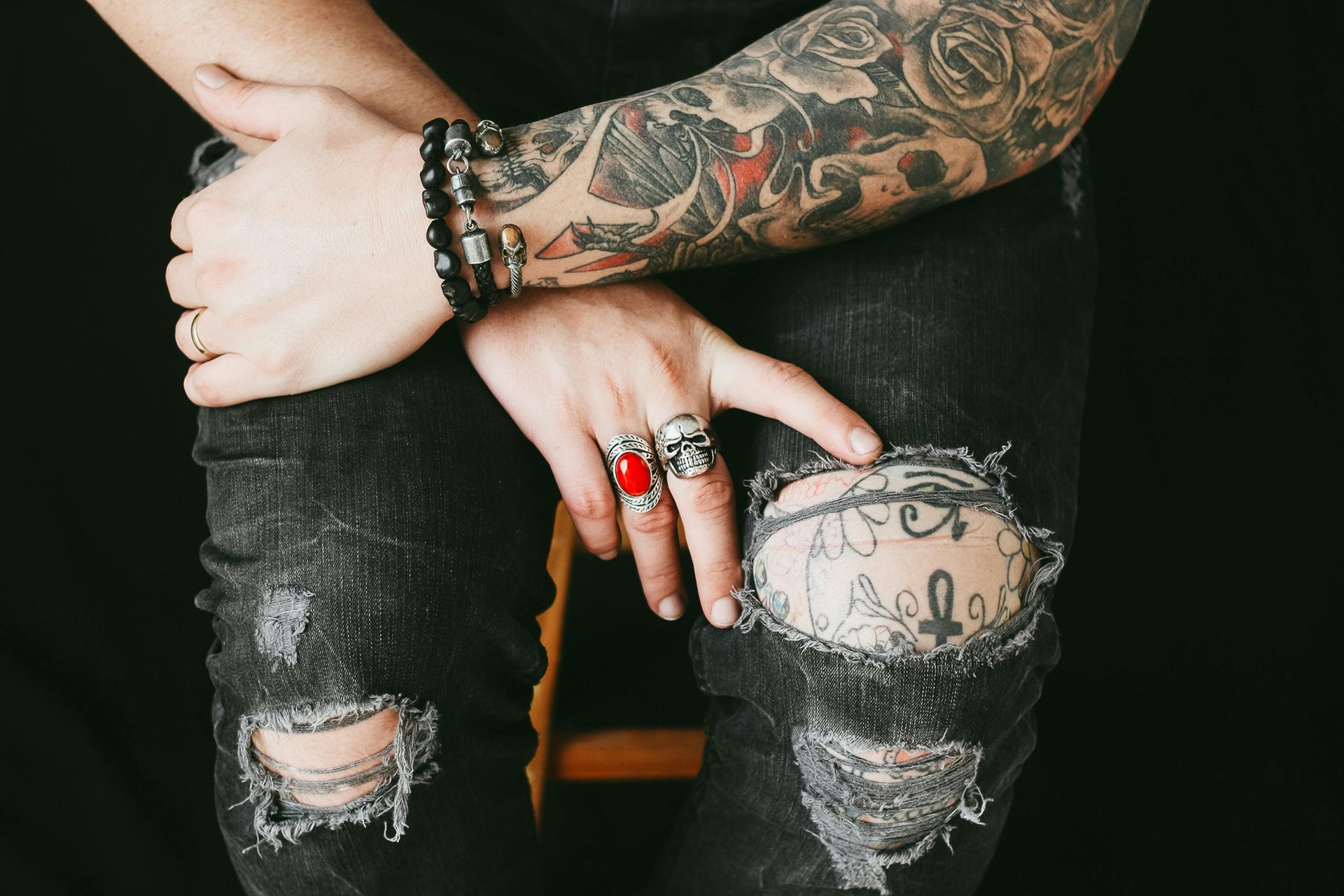 A person with a tattoo on their arm is wearing ripped jeans and rings.