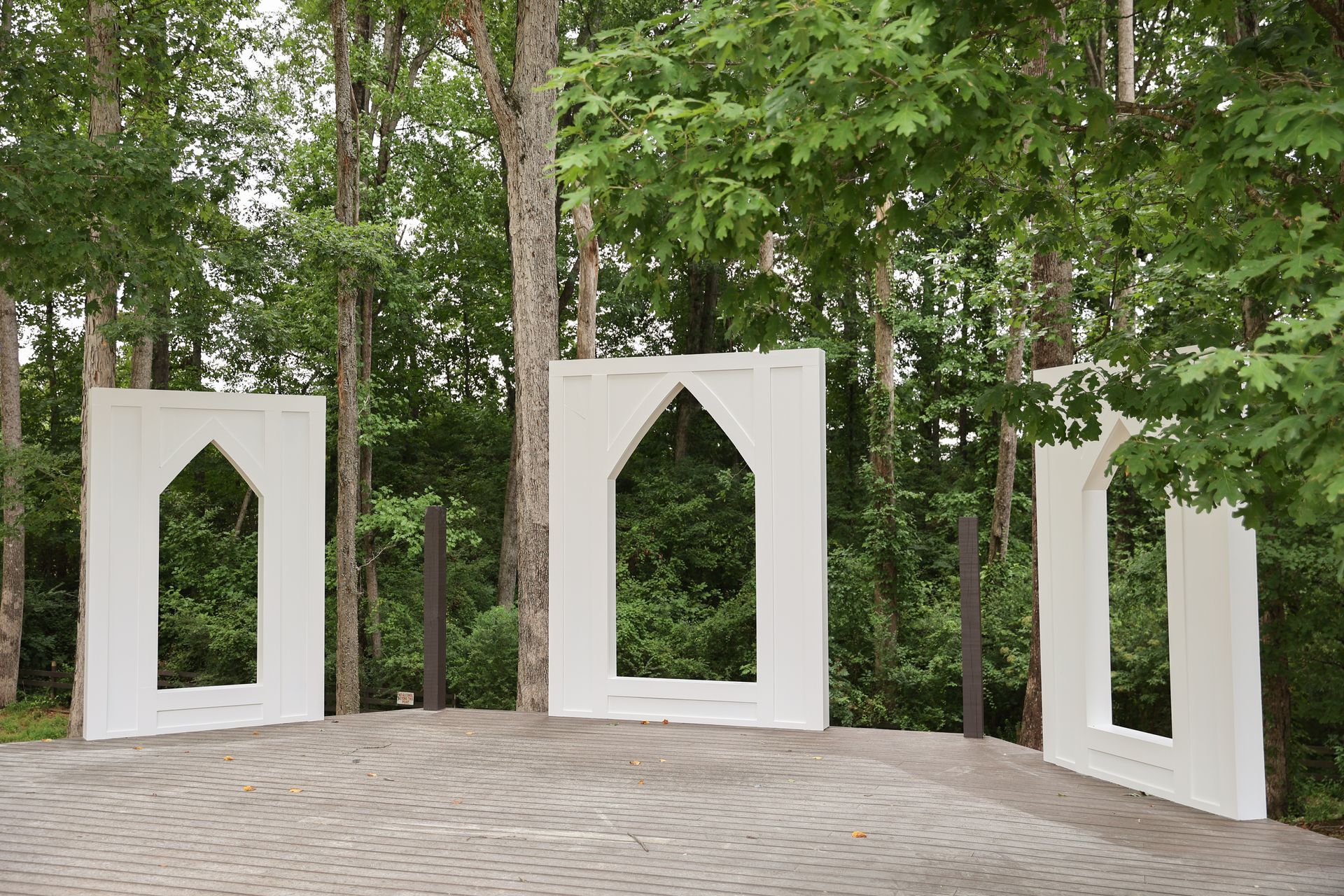 A group of white sculptures in the shape of a house are surrounded by trees.