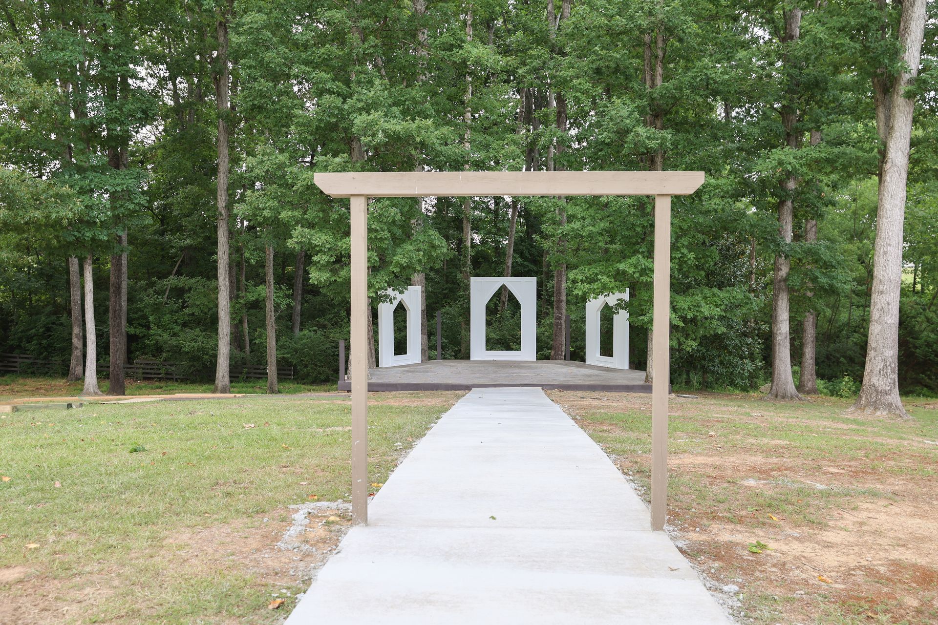 A concrete walkway leading to a wooden archway in the middle of a field.