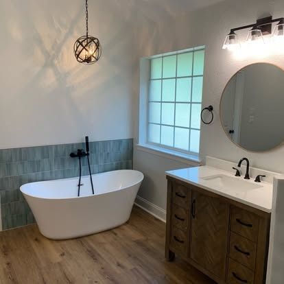 Modern bathroom with freestanding tub, wooden vanity, round mirror, and window.