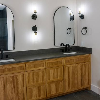 Modern bathroom vanity with wood cabinets, black countertop, double mirrors, and wall sconces