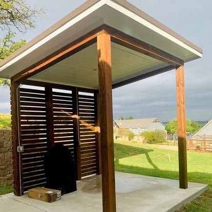 Modern outdoor pergola with wood posts, slatted privacy wall, and concrete floor overlooking a grassy yard