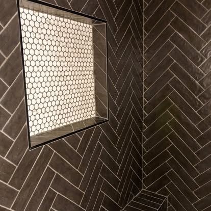 Dark herringbone tile wall with a recessed square niche lined in white hex tile