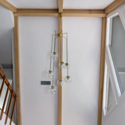 Modern pendant light with glass globes hanging in a stairwell against a white wall and wood beams
