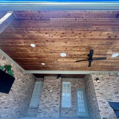 Brick patio with wood-paneled ceiling, black ceiling fan, recessed lights, and white door/windows.